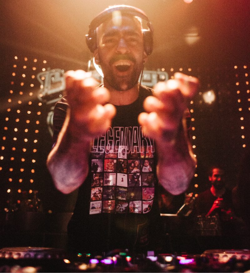 A photo of Harris behind a mixing desk, wearing a headset and laughing as he holds his hands out towards the camera.
