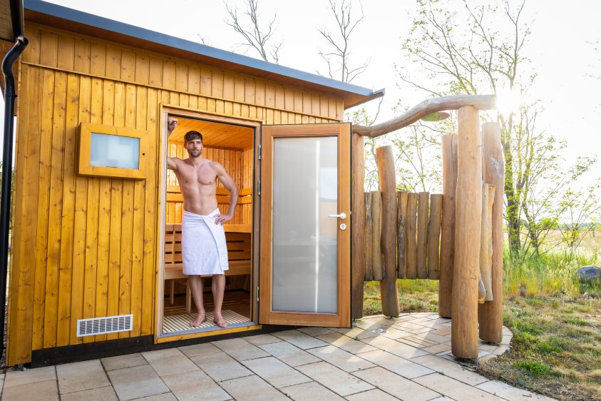 Terrace with seating area, loungers and whirlpool in front of meadow and trees under a clear sky.